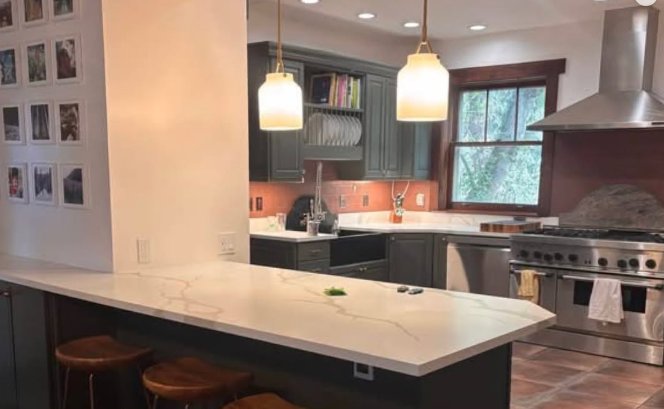 Open kitchen with white quartz peninsula, dark cabinets and pendant lights after a load-bearing wall was removed