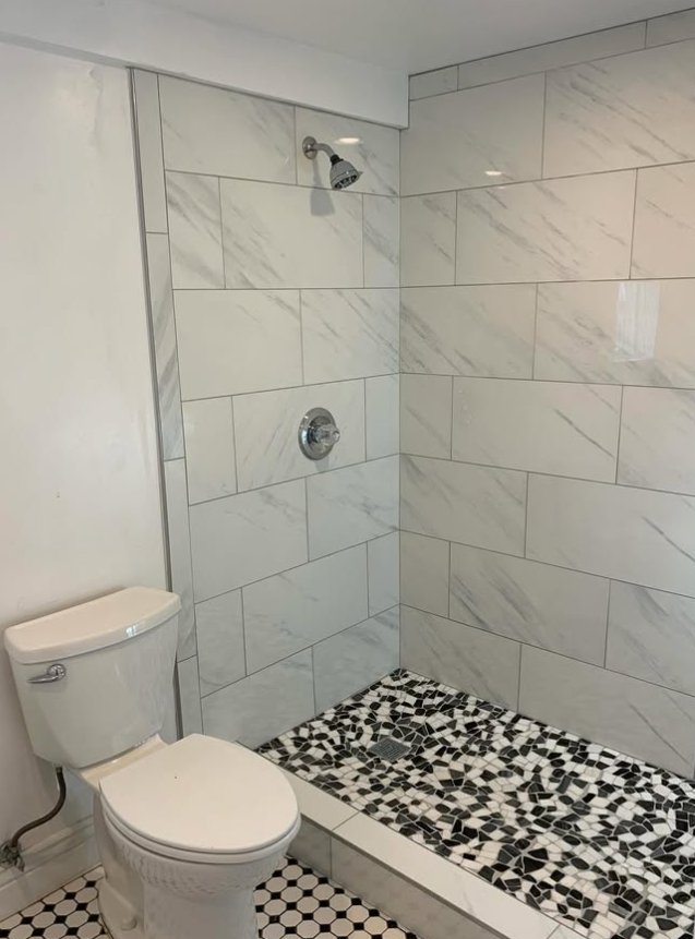 Walk-in shower with large marble-look tile and black and white mosaic floor